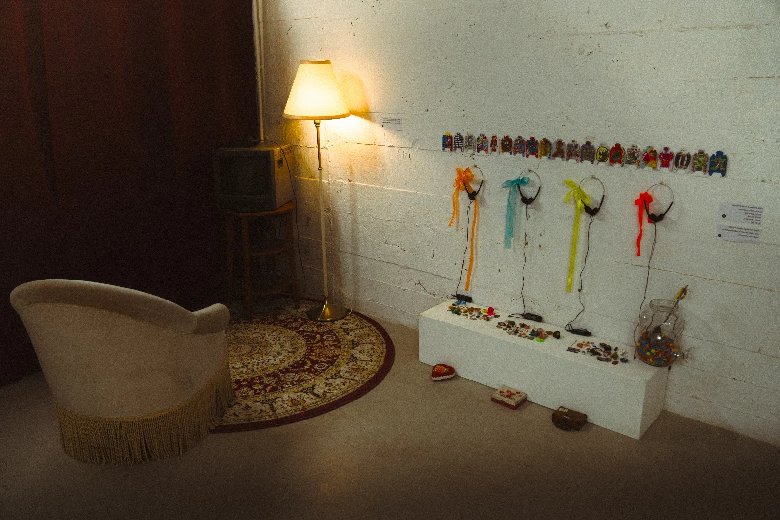 An upholstered chair, floor lamp and rug beside a display of objects and coloured ribbons.