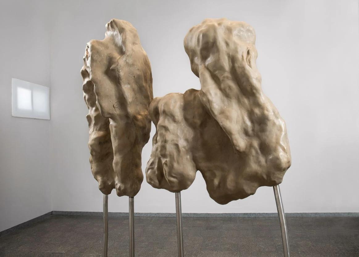An angled exhibition view of the sculptural forms, their textured surfaces and slender metal supports.