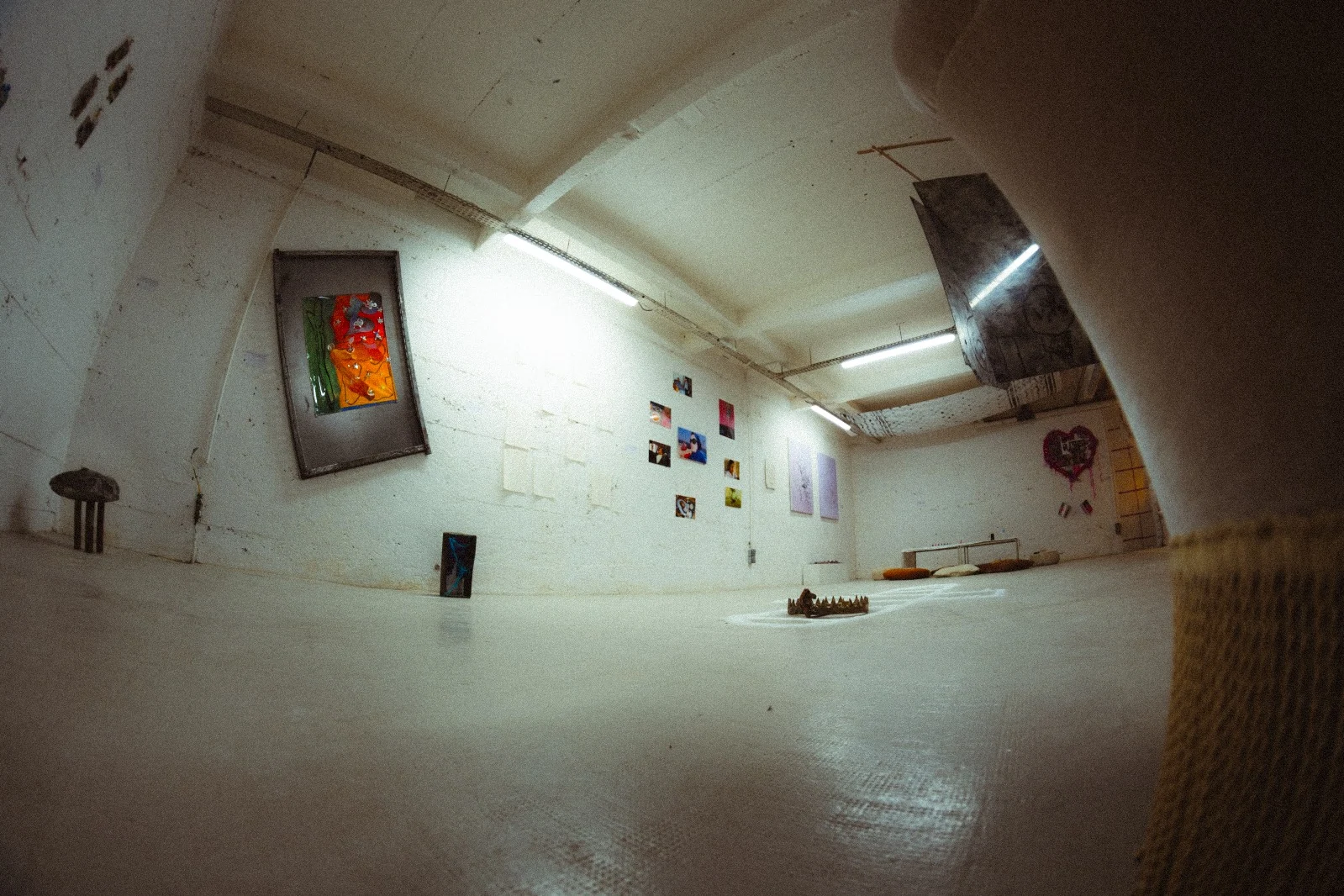 A low viewpoint across the gallery floor toward wall-mounted artworks and small objects.