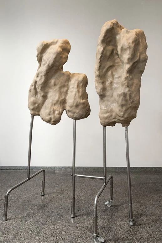 Two sculptures on individual metal stands, photographed from the gallery floor.